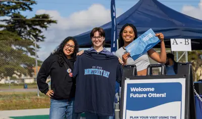 Three students posing for a picture with college merchandise