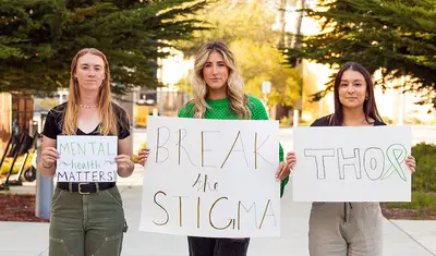 Three student-athletes holding signs in support of mental health advocacy group