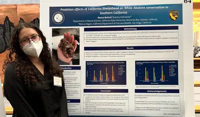 A Hispanic STEM grant recipient stands next to a research poster.