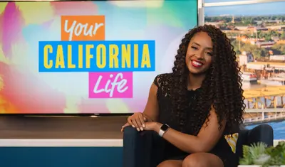 Desiree Sheppard sitting on a couch in front of a TV that shows a text graphic that reads 