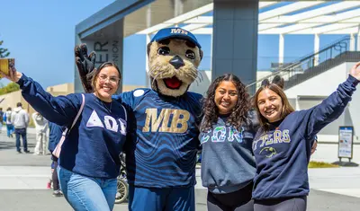 Three students and Monte with their arms around each other on Admitted Otter Day.