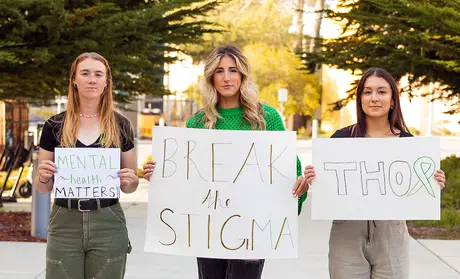 Three student-athletes holding signs in support of mental health advocacy group