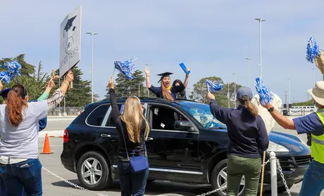 Excited graduate cheering from car while faculty and staff cheer her on