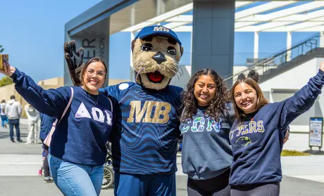 Three students and Monte with their arms around each other on Admitted Otter Day.