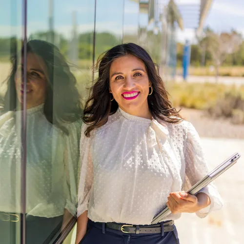 A masters of business administration professor smiling at the camera while leaning against a glass wall