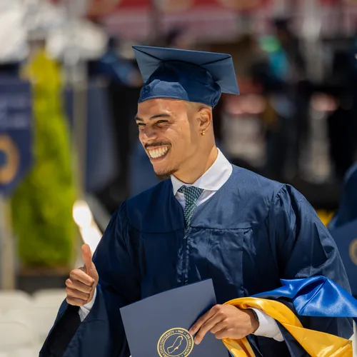 A student in cap and gown holding a diploma in his hand