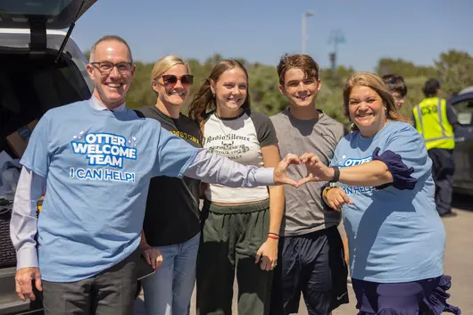 Staff and students form a heart shape with their hands during a campus welcome event, highlighting connection and a supportive community.