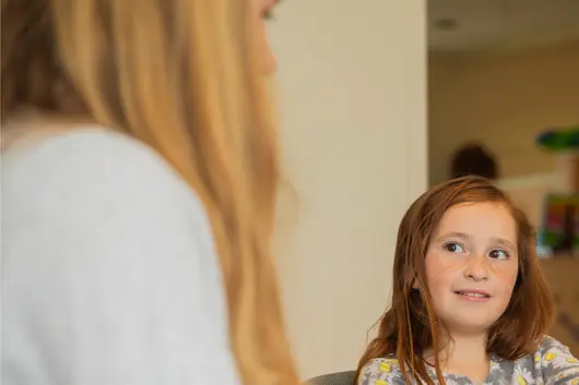A child engages in a learning activity with guidance from an adult, highlighting a supportive and interactive educational environment.