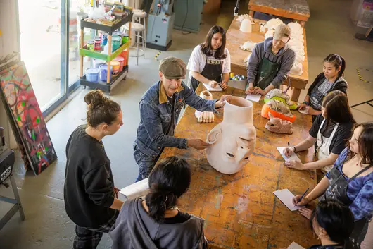 Group of students with instructor holding a pottery ceramic head during a sculpting class
