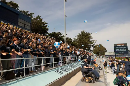 Students gather in stadium seating during a campus convocation event, celebrating community and shared experience.