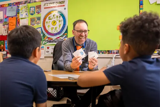 Teacher and students sitting at a table learning shapes and numbers laughing