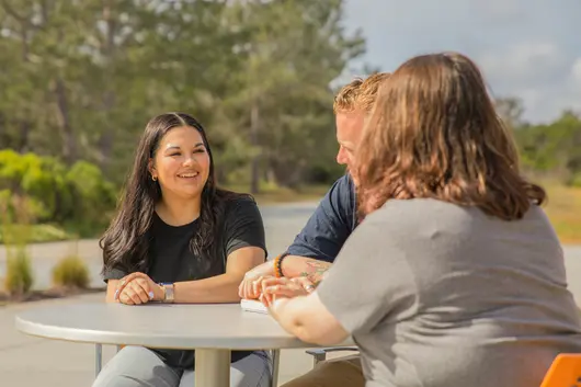 Three students chatting outside while seated at a table