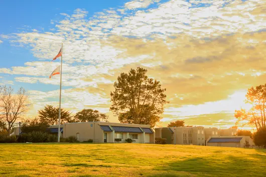 A campus with buildings and flagpole at sunset on a grassy field.