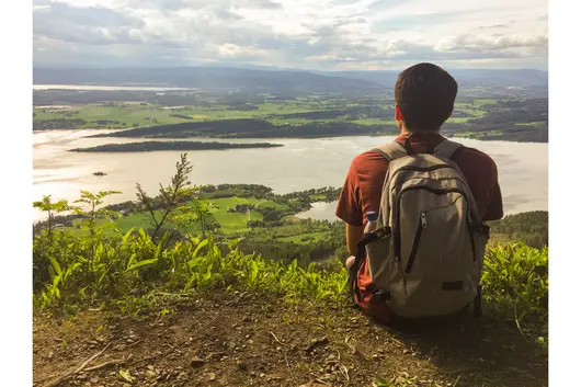 A student sitting down on a hill looking out a green landscape