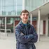 A student standing with his arms crossed and smiling for a portrait in front of a building
