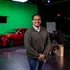 Film crew member posing for photo in front of a green screen and a red car behind him.