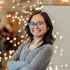 A student standing, smiling at the camera and crossing her arms for a portrait standing in front of some lights