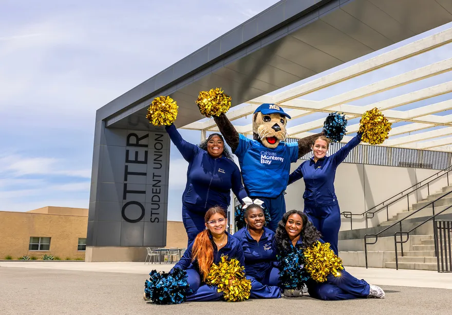 The campus mascot and cheer team pose outside the Otter Student Union, celebrating school spirit and community pride.