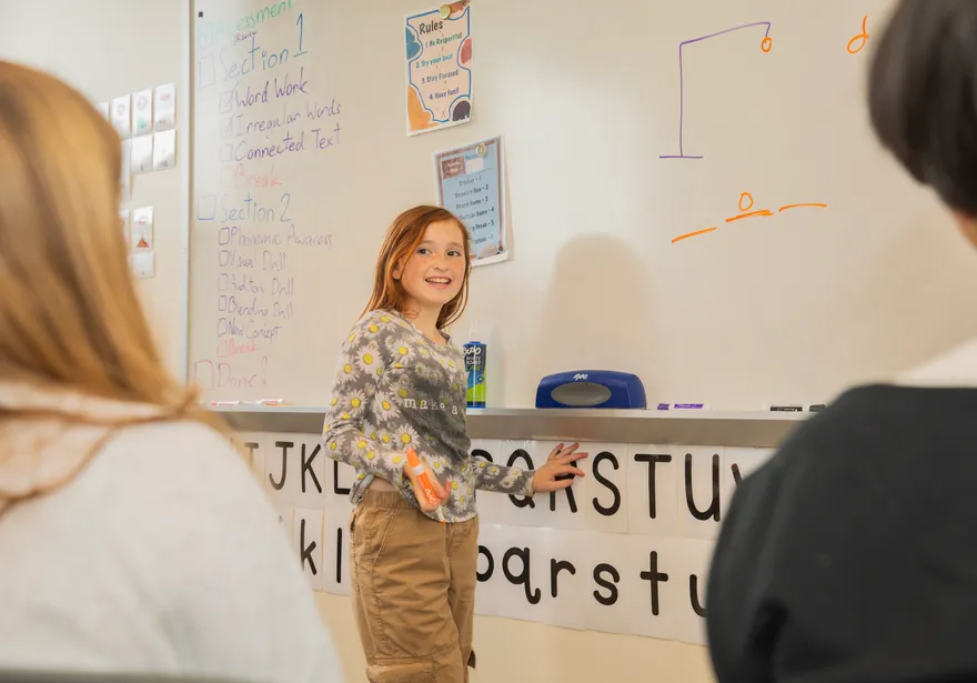 Student presenting in front of a digital whiteboard to students sitting at a table