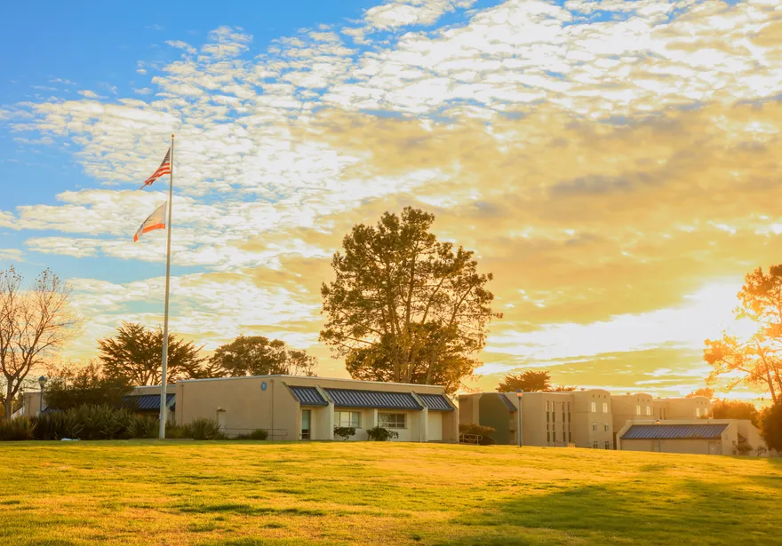 A beautiful sunset casts a golden glow over campus buildings and trees, with flags waving gently in the evening breeze.