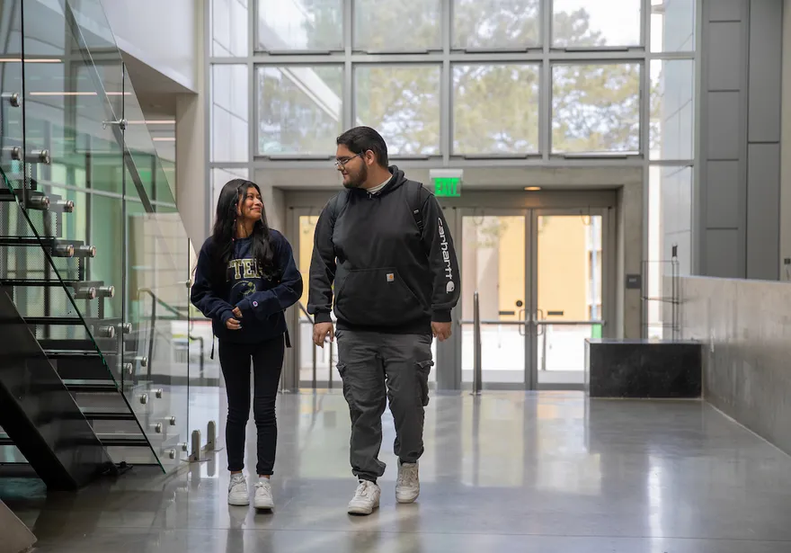 Two students walk and connect in a bright campus building, reflecting a welcoming and supportive learning environment.