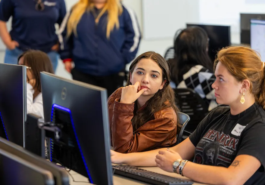 students at a desk in a classroom looking at a monitor