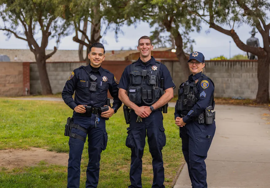 Three CSUMB University Police officers in uniform smile and wave at the camera.