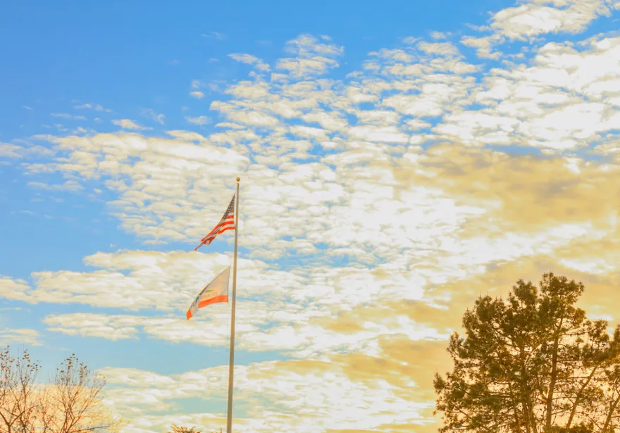 A beautiful sunset casts a golden glow over campus buildings and trees, with flags waving gently in the evening breeze.