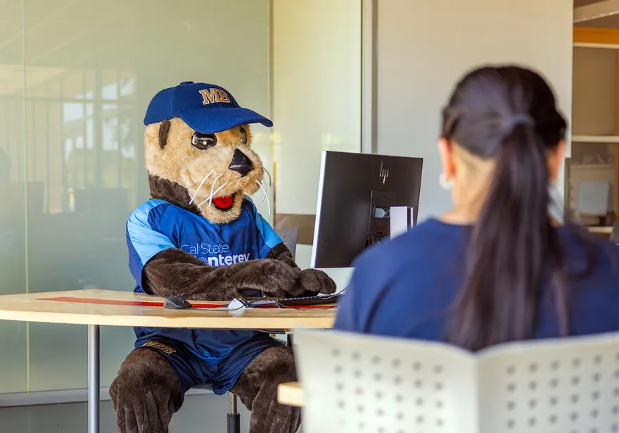 Mascot in front on Computer and a student