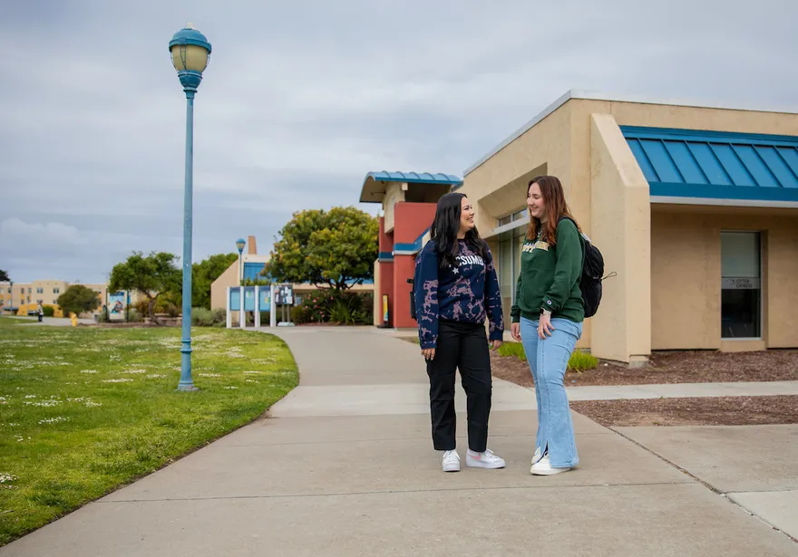 Two students stand and talk along a campus walkway, building connection in a relaxed and welcoming environment.