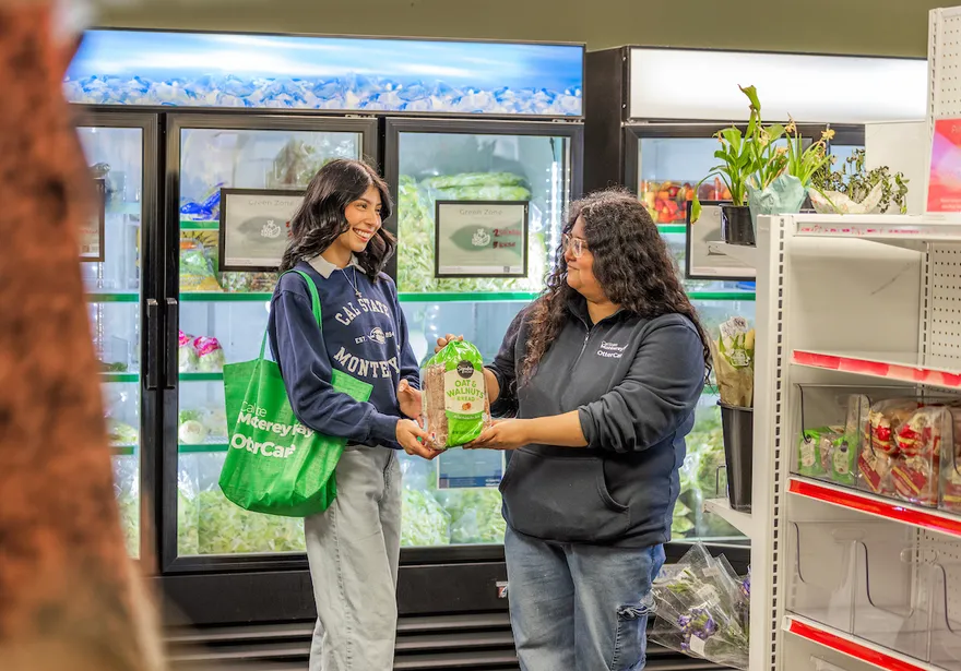 Two people exchanging a grocery item inside the Otter Care pantry.