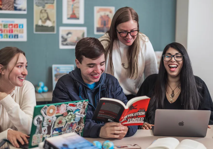 CSUMB Global Studies students laugh and discuss ideas while reading books and using laptops together during a collaborative classroom study session.