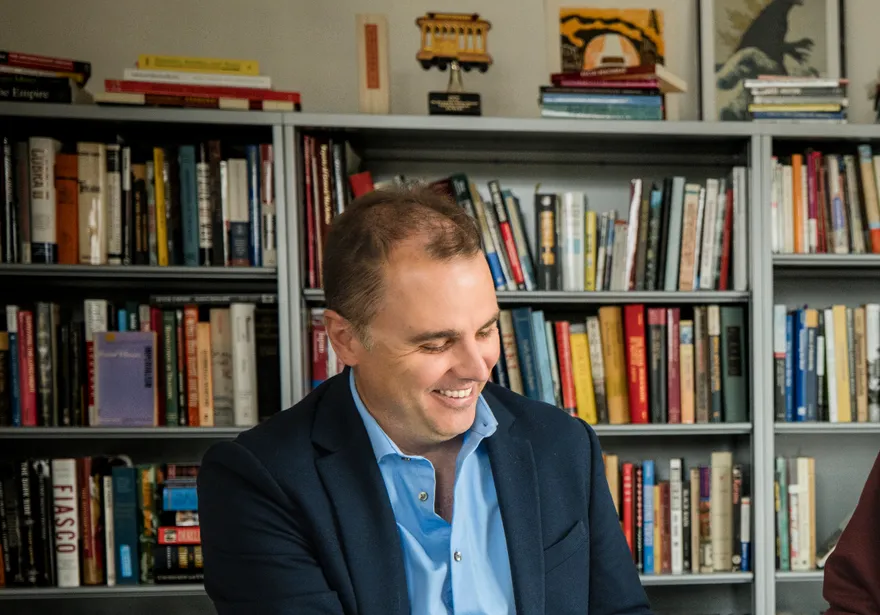 A faculty member and a student sit together at a table in an office lined with bookshelves, smiling as they review Japanese-language books and written materials during an academic discussion.