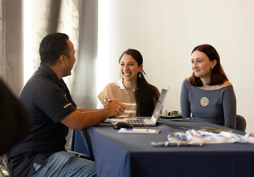 3 students sitting at a table with laptops