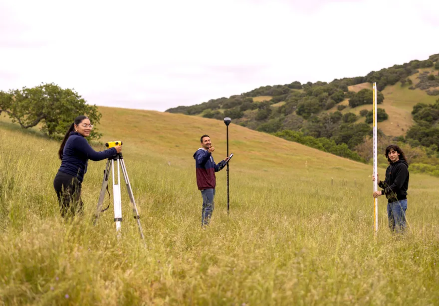 A group of three AES students setting up surveying tools in the grass