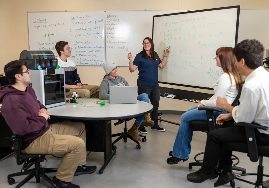 A professor giving a presentation to students sitting by a 3d printer