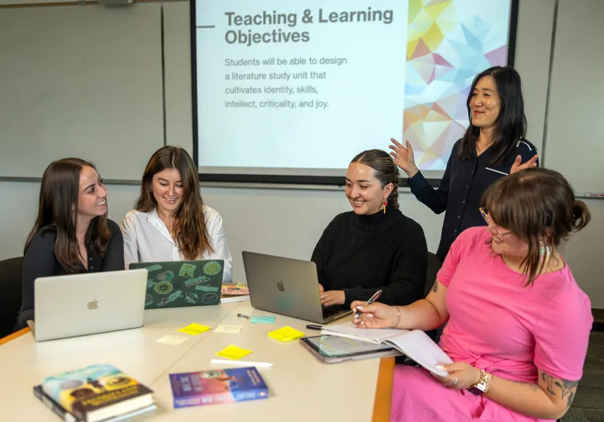 Four students sitting at a table listening to their professor teach them.