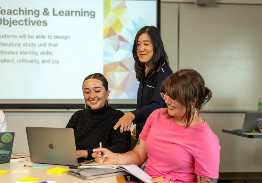 A professor helping two students with their work while they sit at a table together.