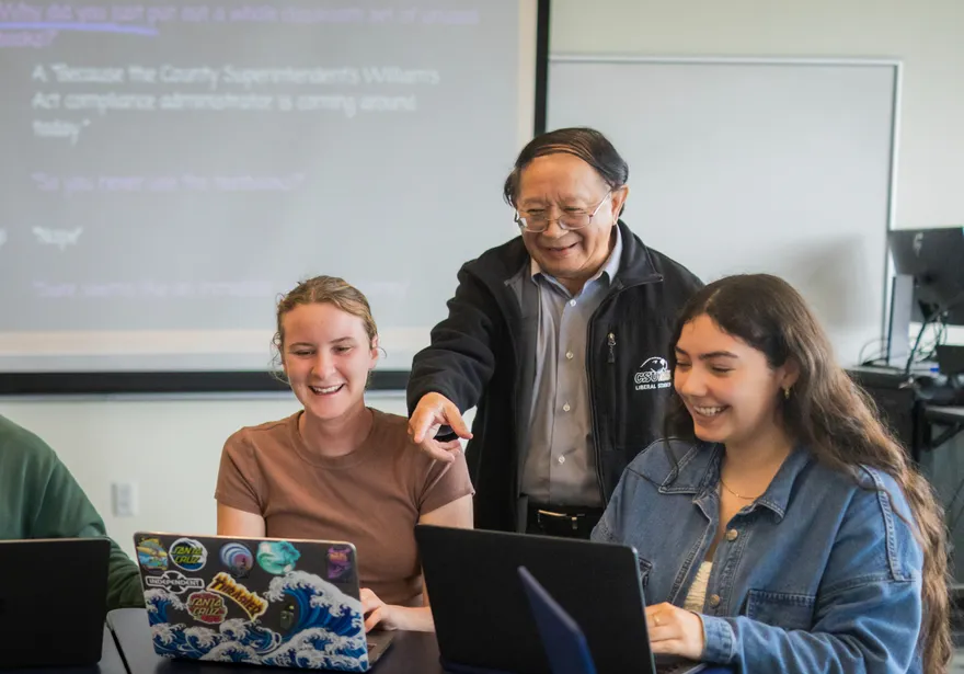Professor points at a student’s laptop while three students discuss and work together in class