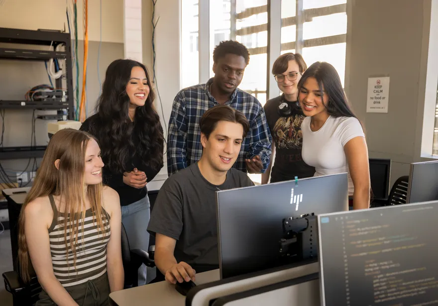 A group of students looking at a students desktop while they work on it