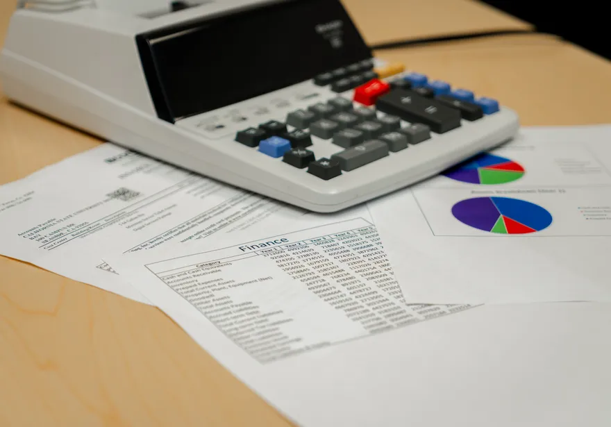 Close-up of financial reports, printed spreadsheets, and pie charts labeled “Finance,” placed on a desk with a calculator used for budget review at CSUMB.