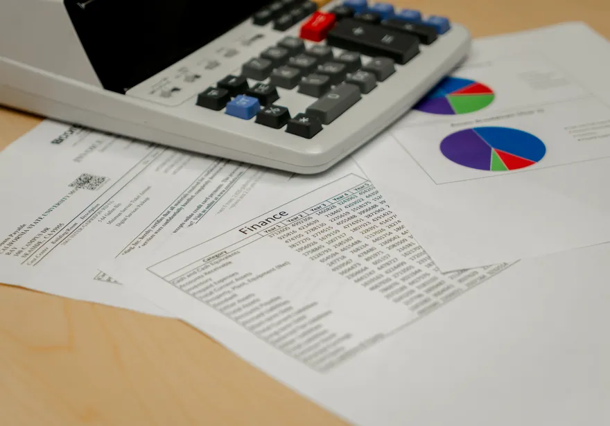 A tabletop view of printed financial documents and colorful pie charts beneath a calculator during budget review at CSUMB’s Finance Department.