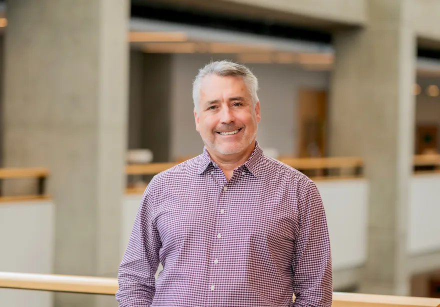 Portrait of the CSUMB Ombuds smiling, standing indoors with blurred university building background.