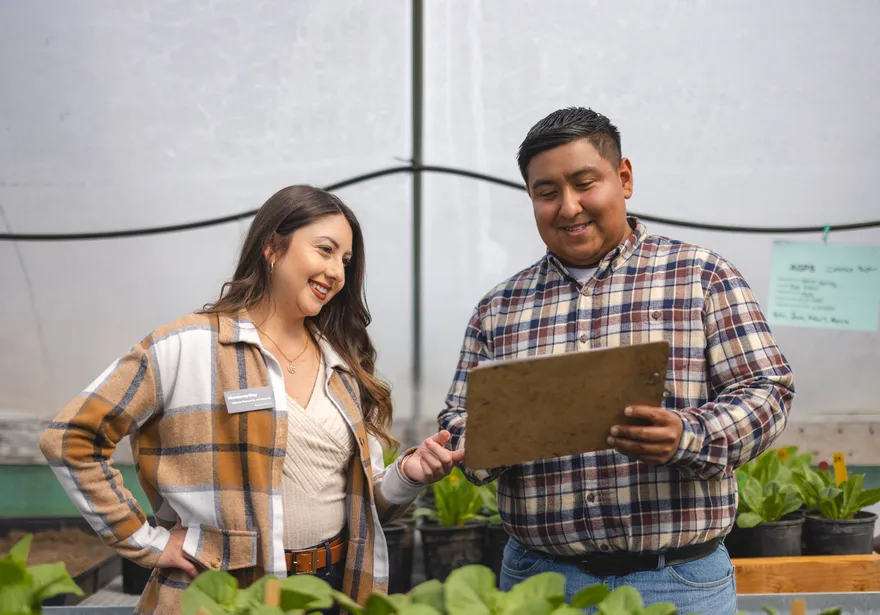 An agriculture science student and professor look at a clipboard amidst greenery