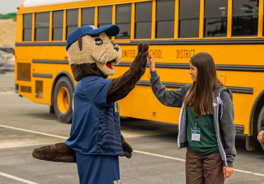 Mascot high fiving a student in front of a bus