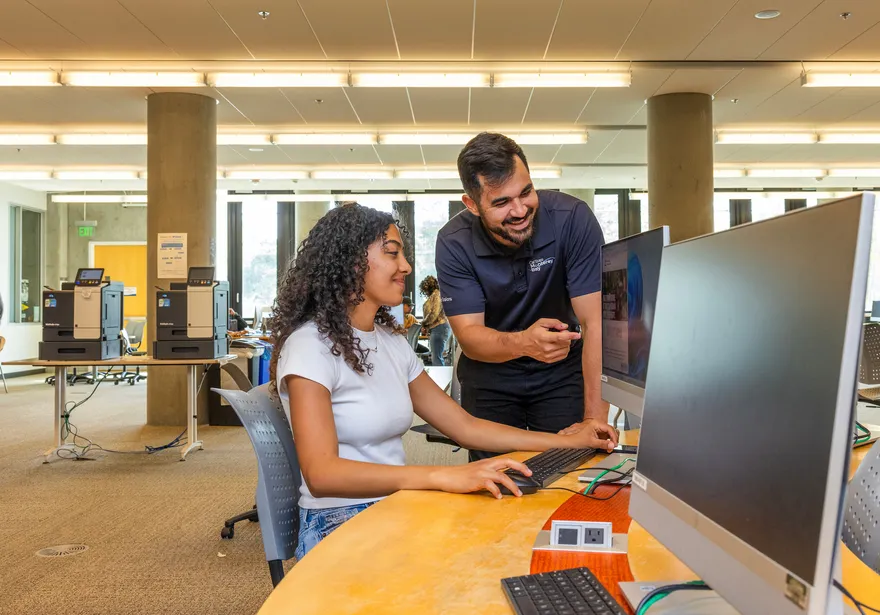 Student getting advise while seated at computer in library