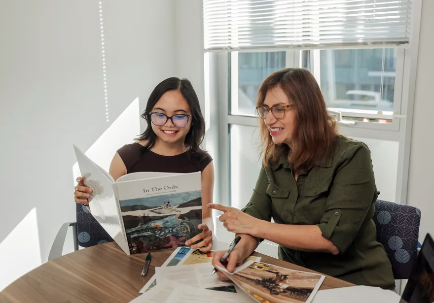 Student holding up a book smiling while the professor is pointing at it