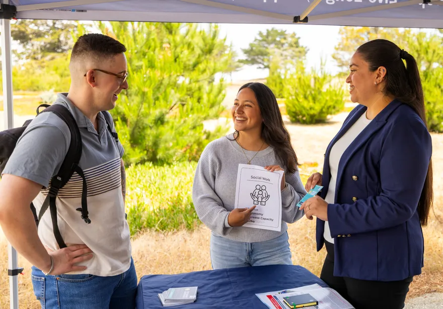 Two people showing a student a social work flyer while smiling and pointing at it.