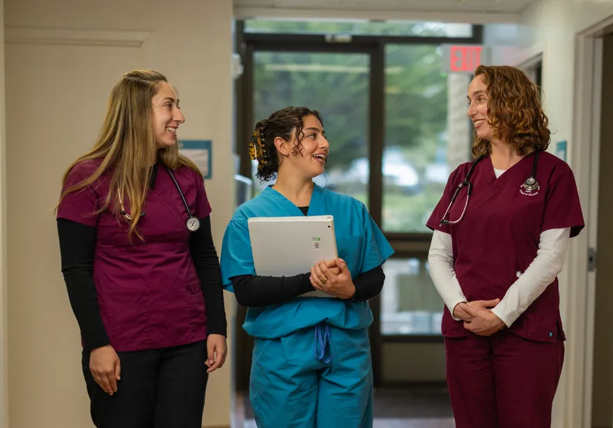 A group of three nursing students in scrubs standing together in a walkway talking together