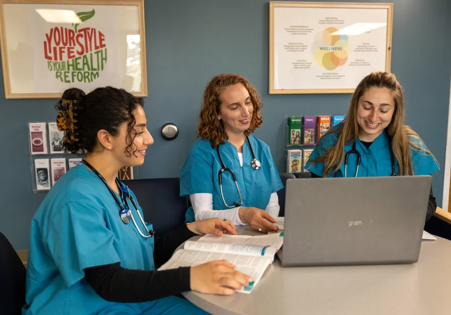 A group of three nursing students in scrubs sitting down at a table collaborating together
